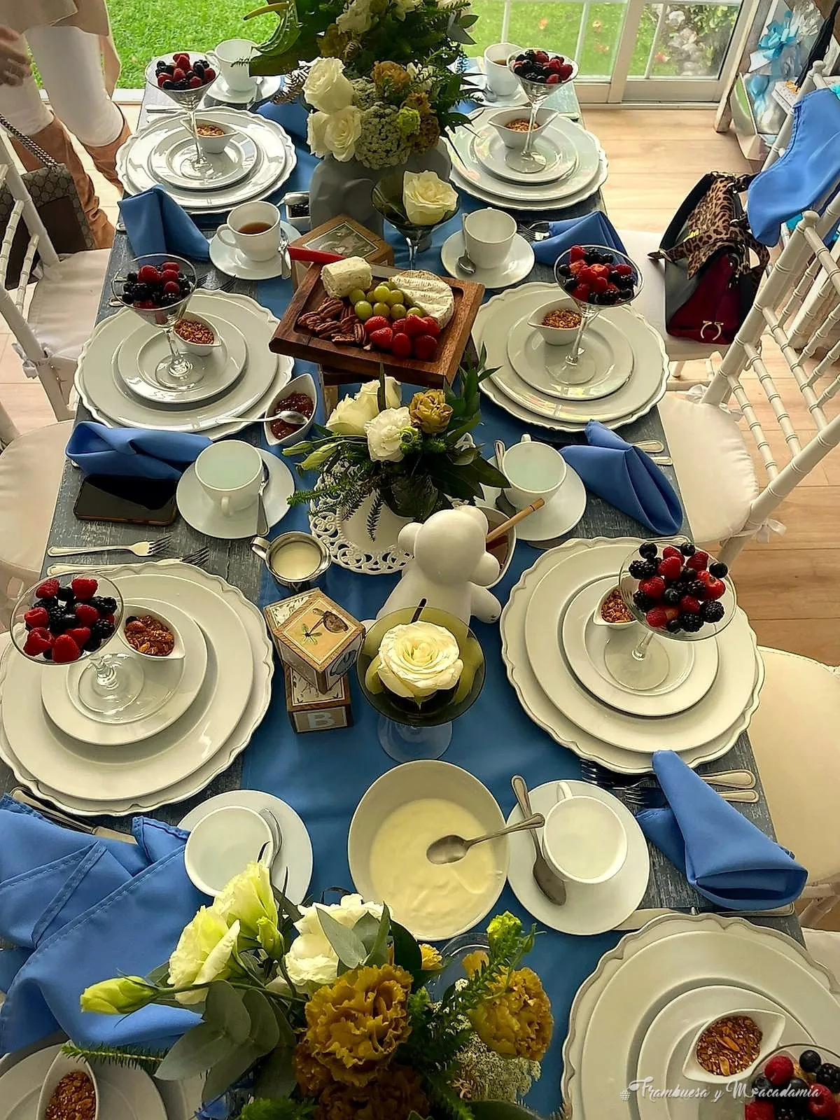 Mesa de desayuno montada en azul con parfaits de frutos rojos, granola y flores para baby shower