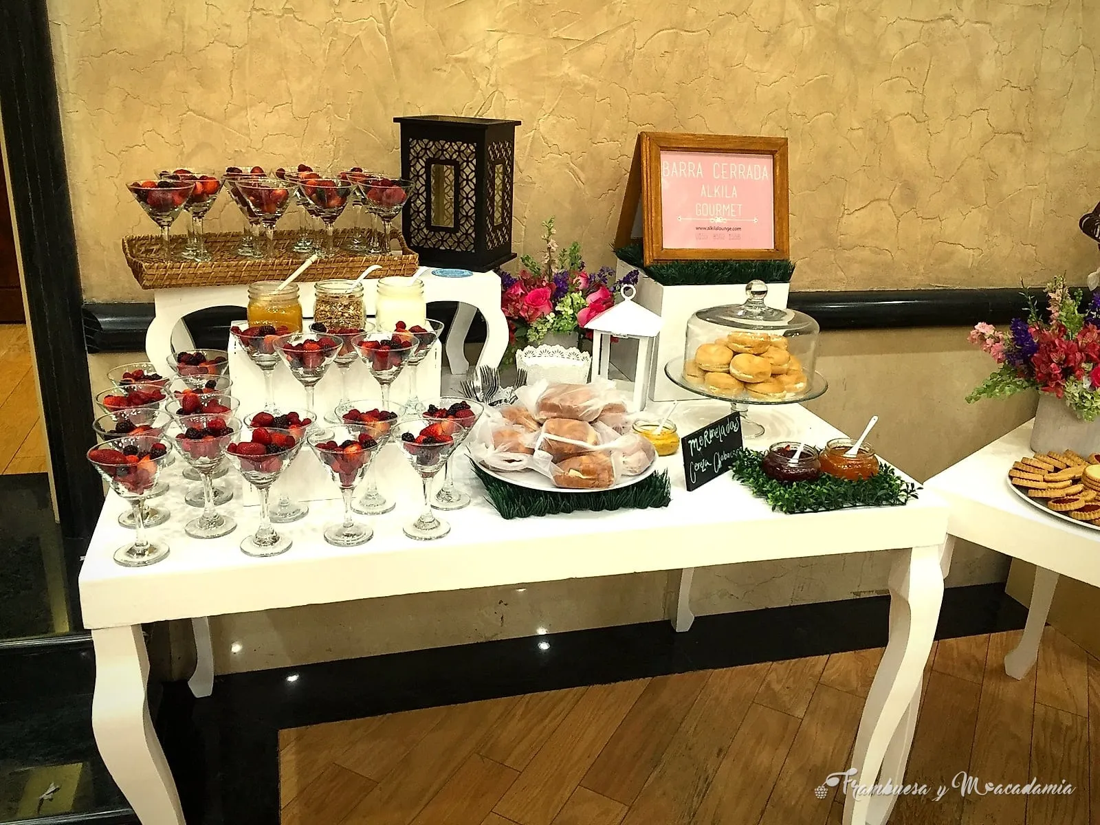 Mesa blanca de coffee break con copas de frutos rojos, galletas y flores