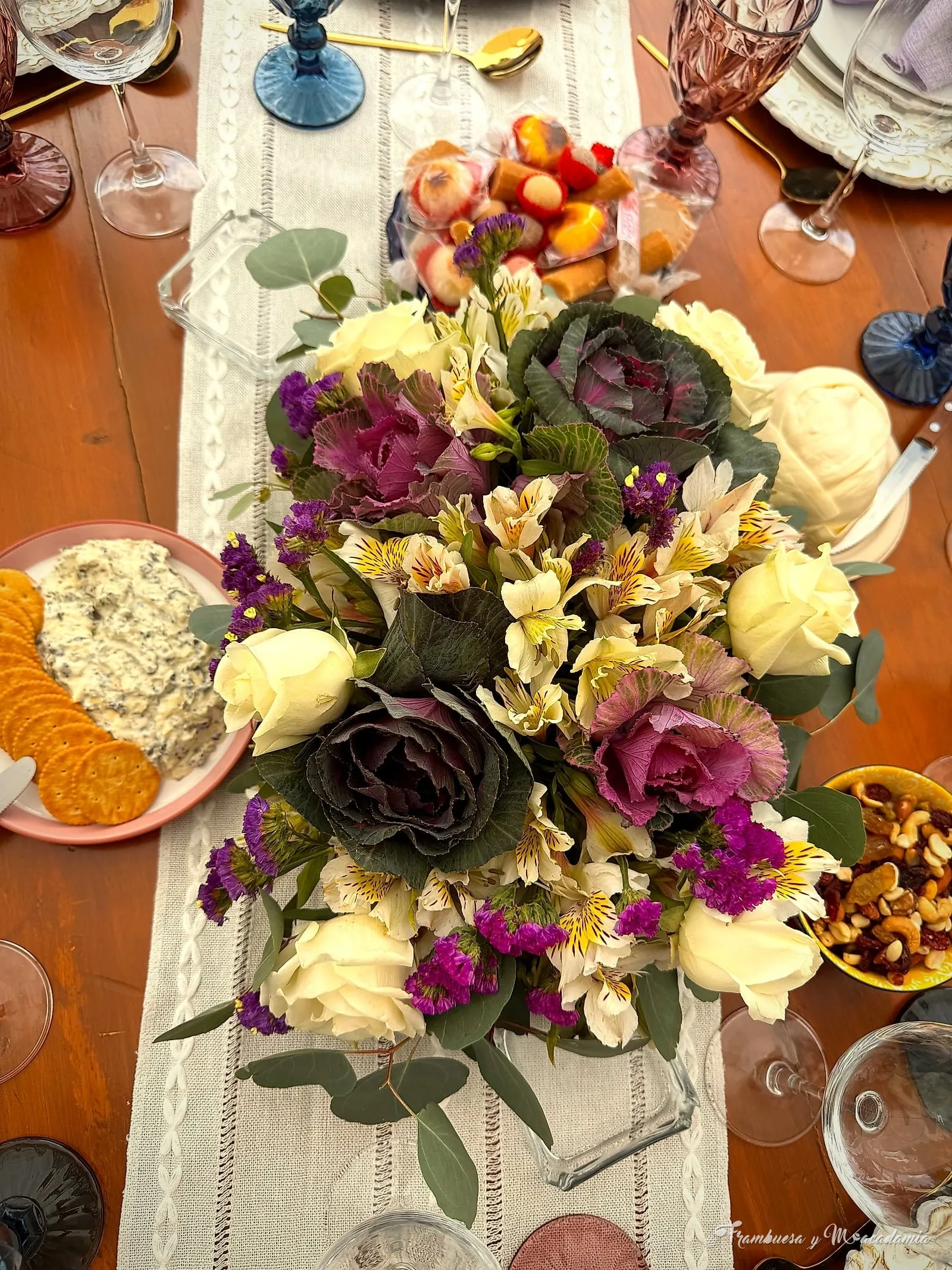 Mesa puesta con camino de tela, copas de colores y centro de flores