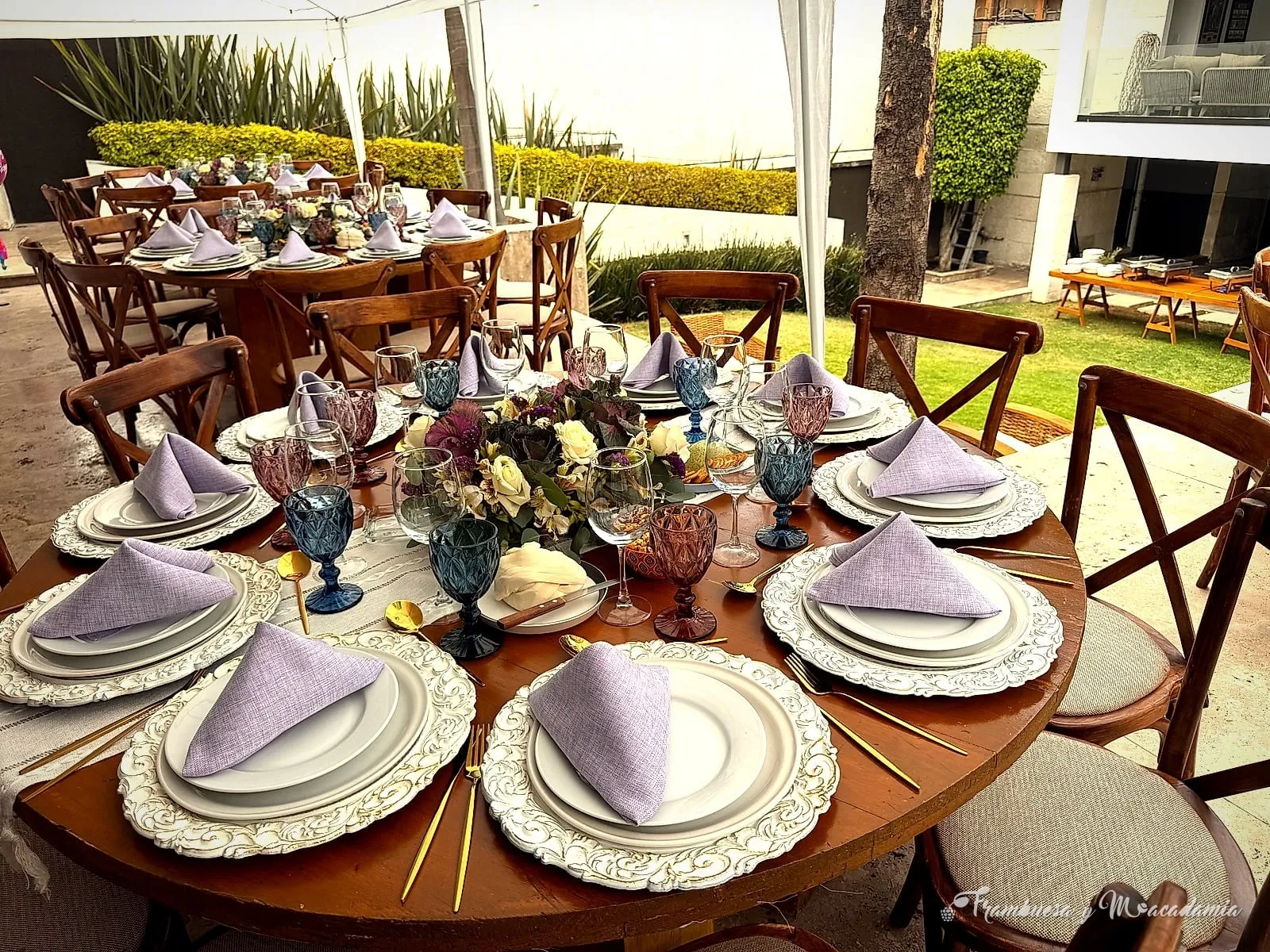 Mesa redonda montada con plato base, cristalería de color y servilletas lilas