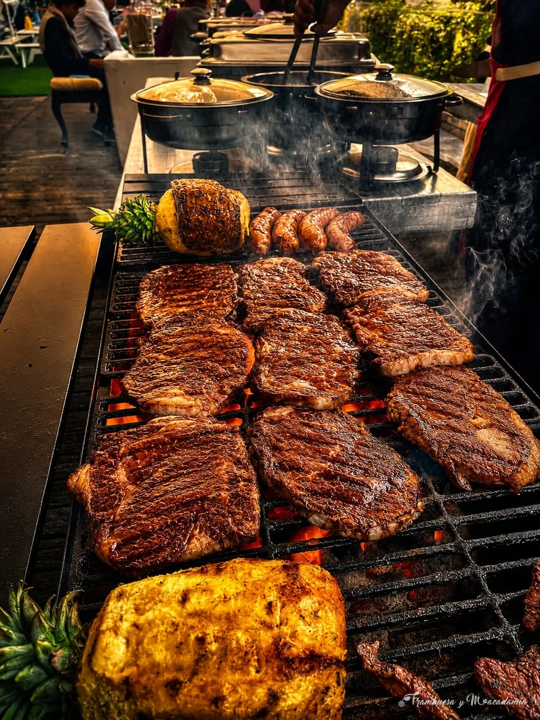 Cortes de carne asándose al carbón con elote y chorizos al fondo