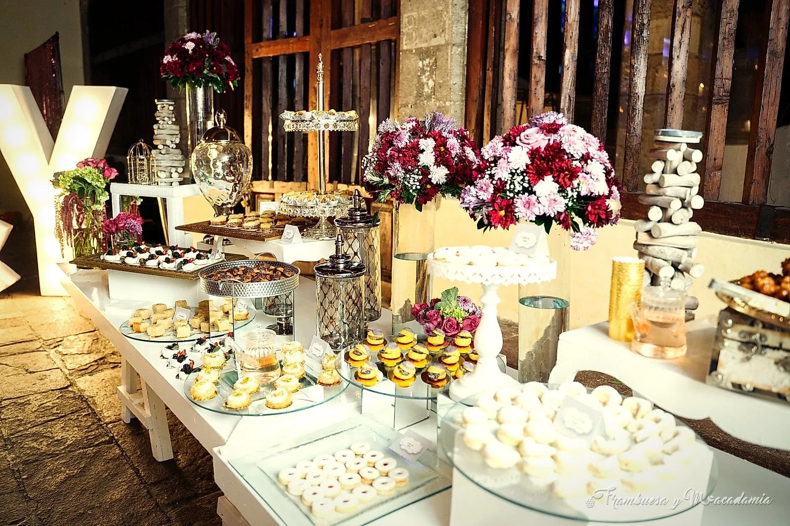 Mesa de postres de boda con letra luminosa, flores en tonos vino y torres de dulces