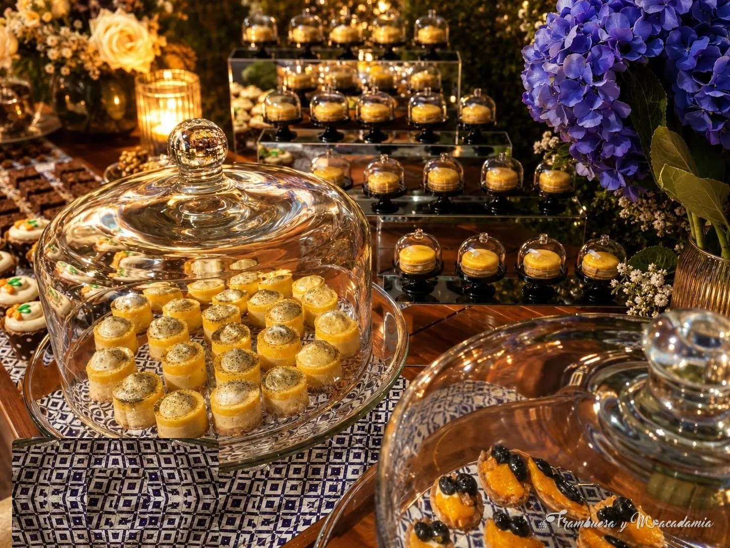 Mesa de postres con campanas de cristal, mantel de talavera y hortensias azules